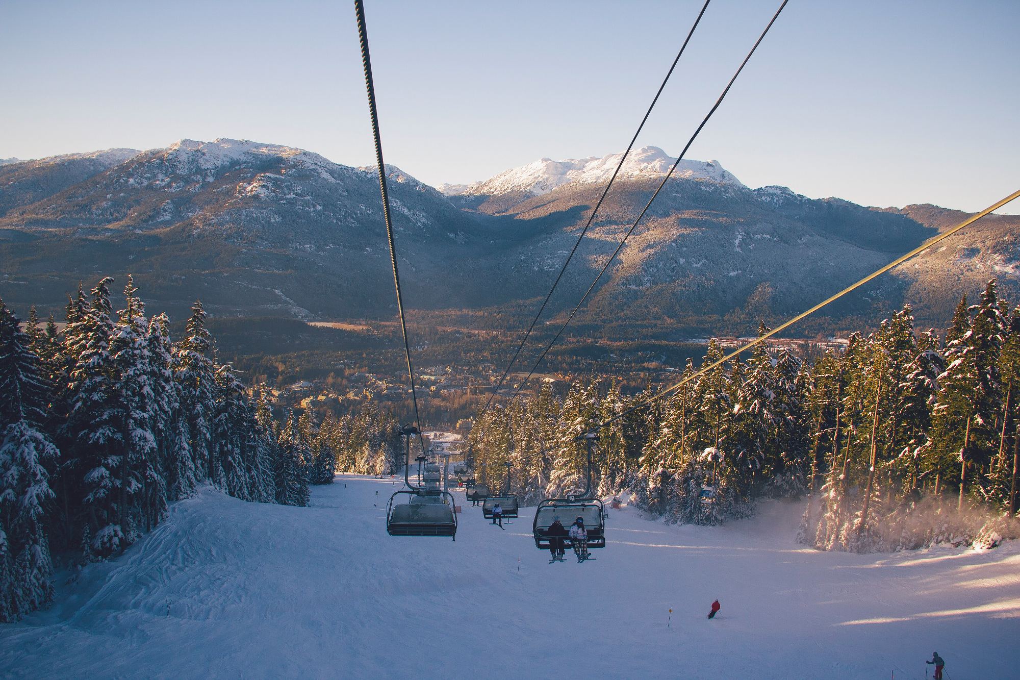A chairlift running down into a snowy valley in golden light, mountains behind